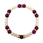 A beaded stretch bracelet featuring alternating deep magenta-purple and cream-colored porous beads, accented by small gold spacer rings with clear rhinestones, set against a plain white background.