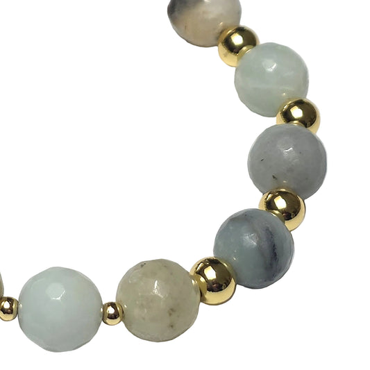 A close-up of a beaded strand featuring large pale greenish-gray stone beads and smaller polished gold spacer beads on a white background.