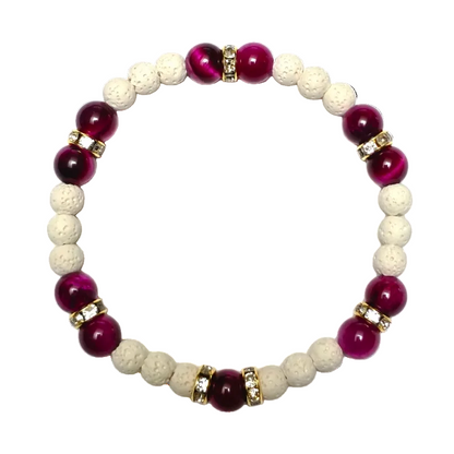 A beaded stretch bracelet featuring alternating deep magenta-purple and cream-colored porous beads, accented by small gold spacer rings with clear rhinestones, set against a plain white background.